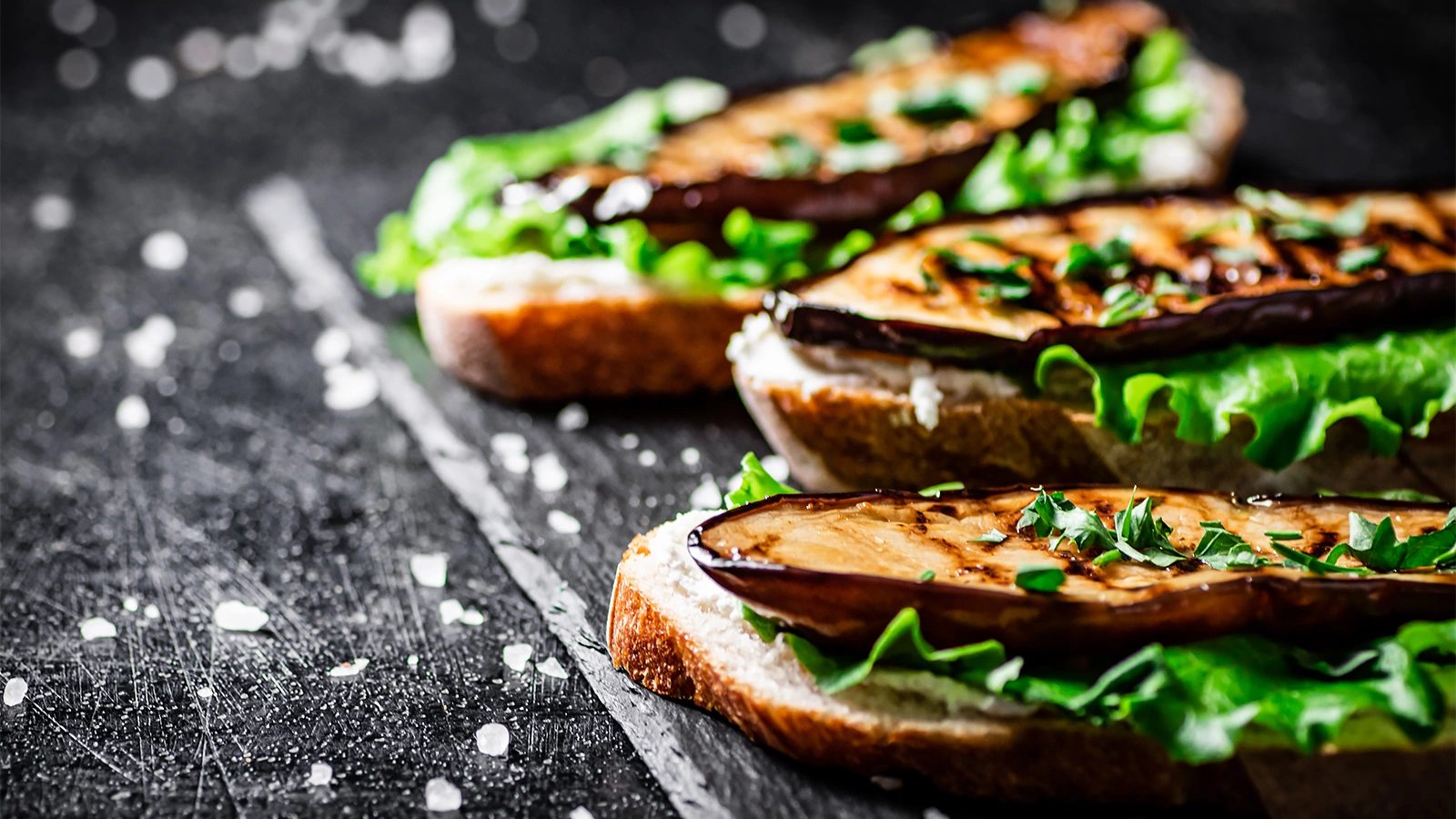 <p>Caption: Grilled eggplant sandwich on a stone board. On a black background</p>
