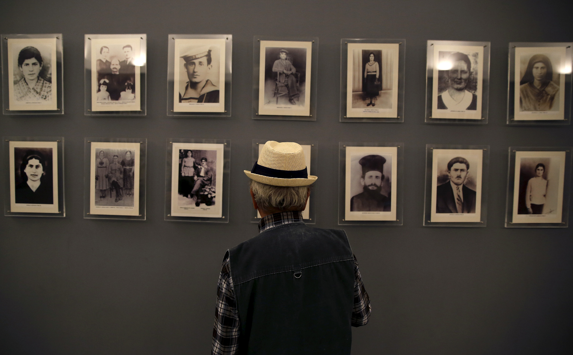 Родственник жертв нацистской оккупации смотрит на мемориальную стену с фотографиями погибших