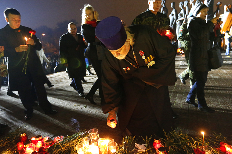 Священнослужитель ставит свечу к памятнику узникам фашистских концлагерей на Поклонной горе во время акции скорби по убитым мирным жителям в Донецкой области.&nbsp;