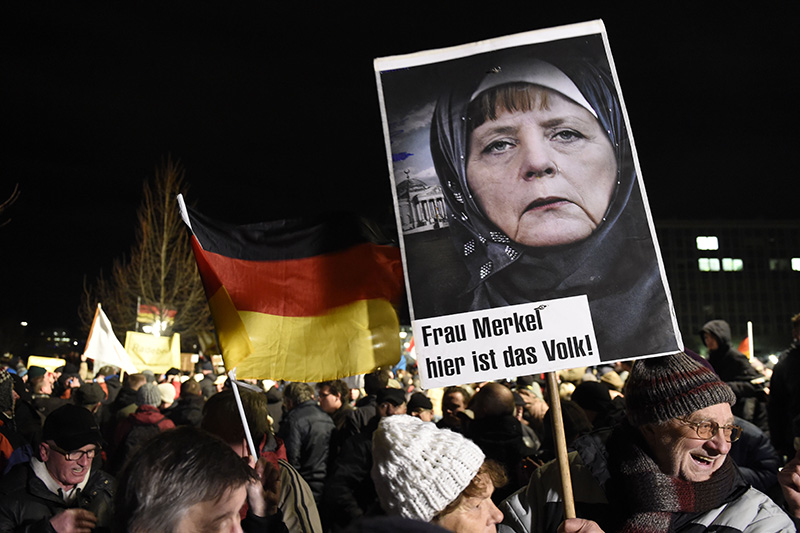 Сторонник ПЕГИДА на акции против исламизации Европы 12 января держит плакат с портретом канцлера Германии Ангелы Меркель и подписью: &laquo;Госпожа Меркель, народ здесь&raquo;.