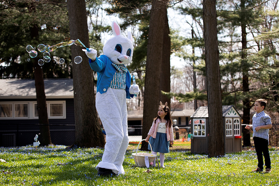 Человек, одетый как пасхальный кролик, пускает мыльные пузыри с трехлетней девочкой во время празднования Пасхи
