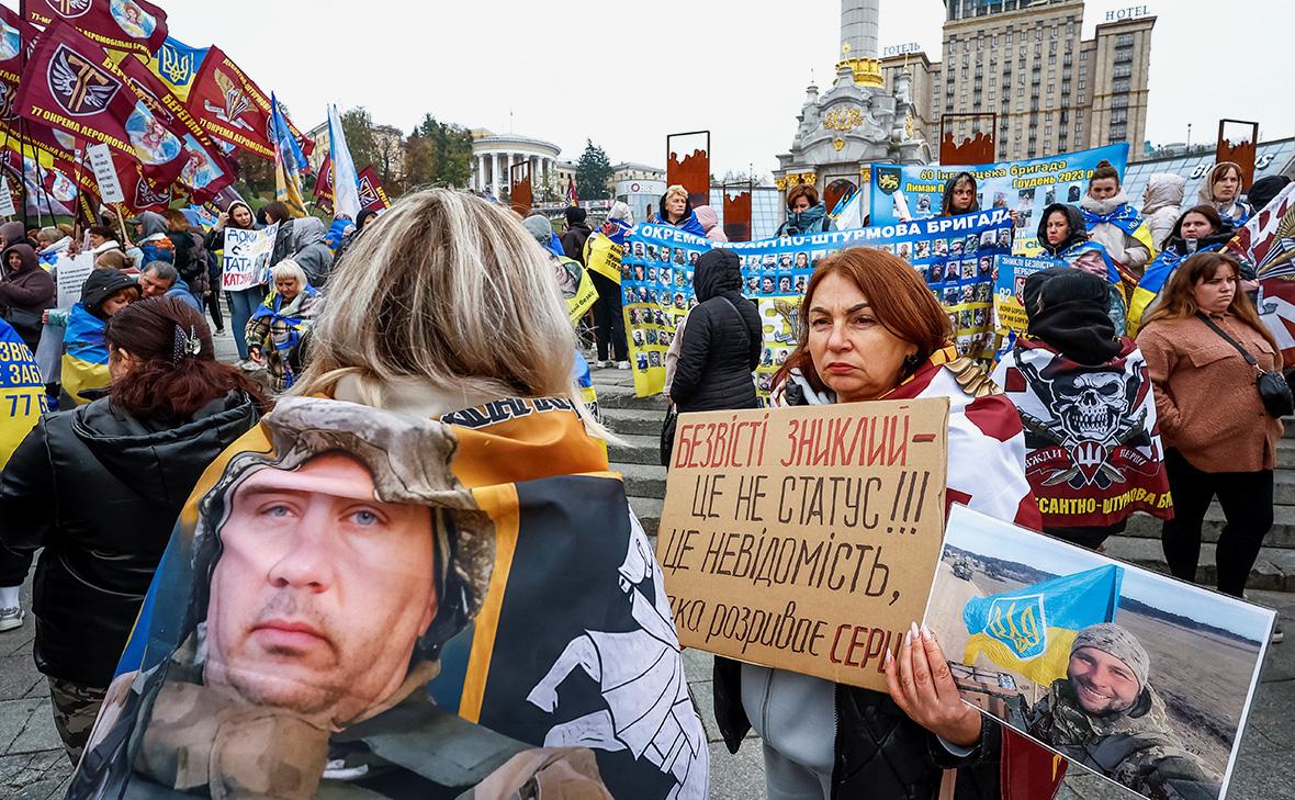 Родственники пропавших без вести украинских военнослужащих держат в руках фотографии членов своей семьи и транспаранты на митинге, 16 октября 2024 года