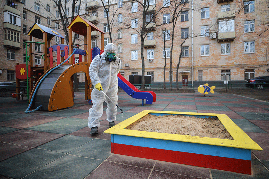 Сотрудник коммунальной службы в защитном костюме и респираторе во время дезинфекции детской площадки, Москва