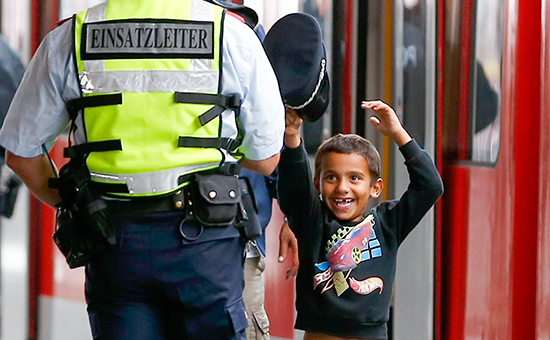 Маленький мигрант примеряет фуражку сотрудника полиции на вокзале в Мюнхене
