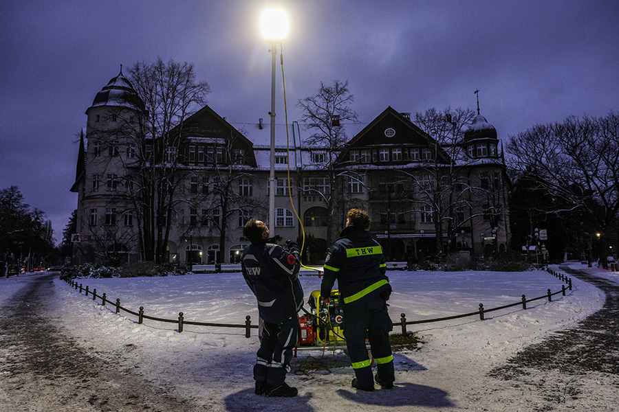 Добровольцы Федерального агентства технической помощи Германии зажигают уличный фонарь, работающий от генератора, возле площади Мехикоплац в Берлине