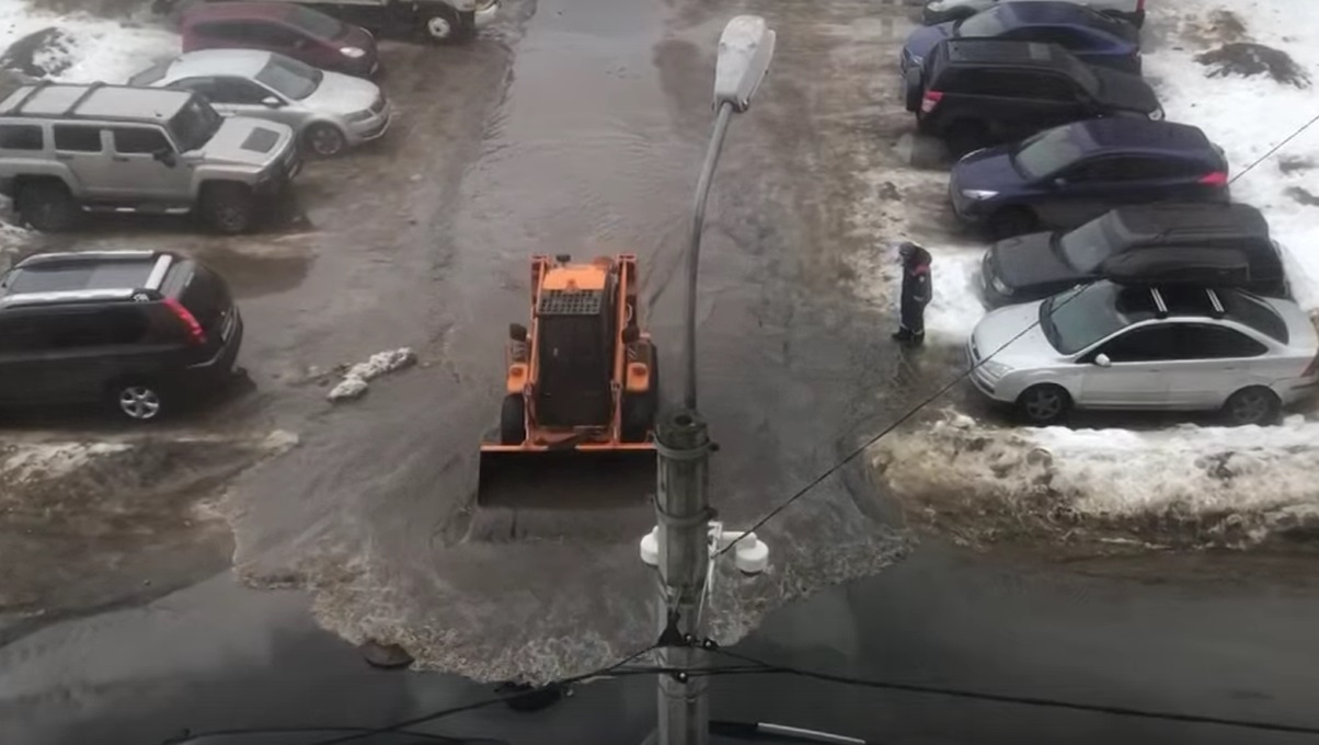 Экскаватор загоняет воду из лужи в сливной колодец