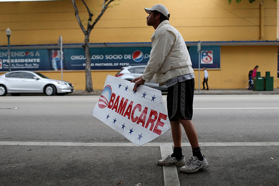 Мужчина держит табличку, направляющую людей в страховую компанию, где они могут подписаться на программу доступного медицинского обслуживания, также известную как Obamacare, 2015 год