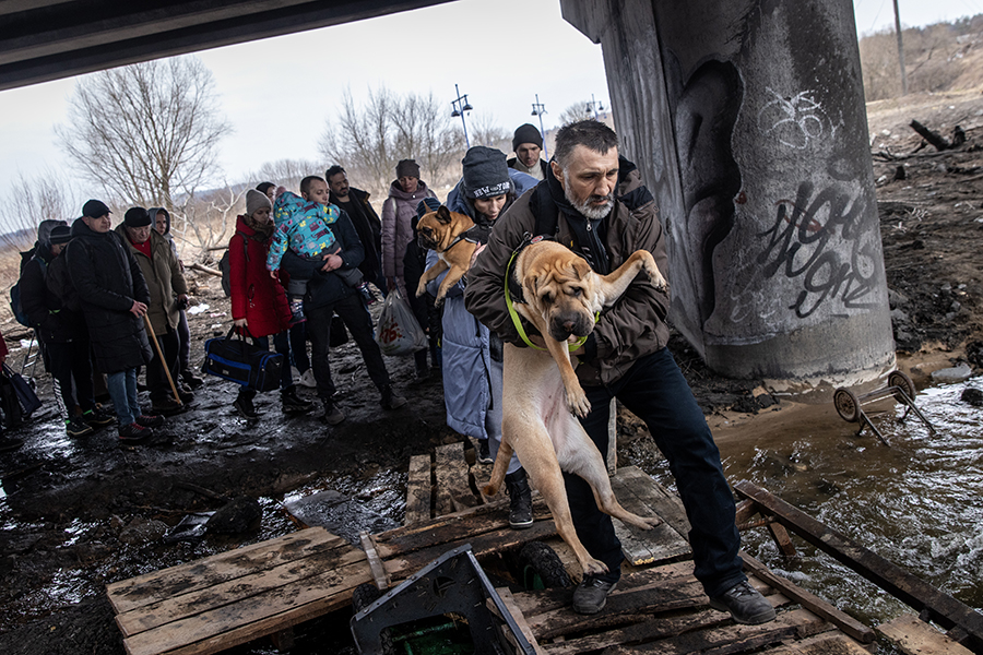 Люди несут на руках своих собак под разрушенным мостом во время эвакуации из Ирпеня, Киевская область, 7 марта
