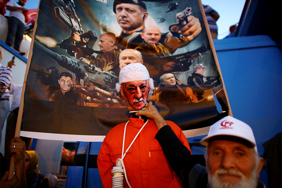 Мужчина в Стамбуле позирует во время церемонии, посвященной первой годовщине неудачной попытки государственного переворота в Турции, с баннером, изображающим исламского проповедника Фетхуллаха Гюлена. Именно его турецкие власти обвиняют в организации мятежа.
