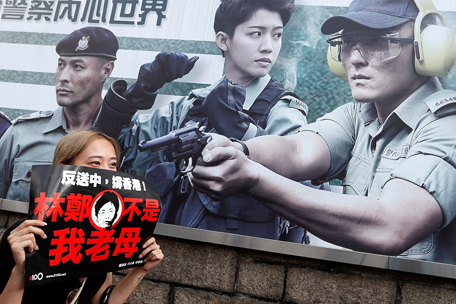 Участница протестов 16 июня на фоне баннера о наборе в полицию Гонконга
