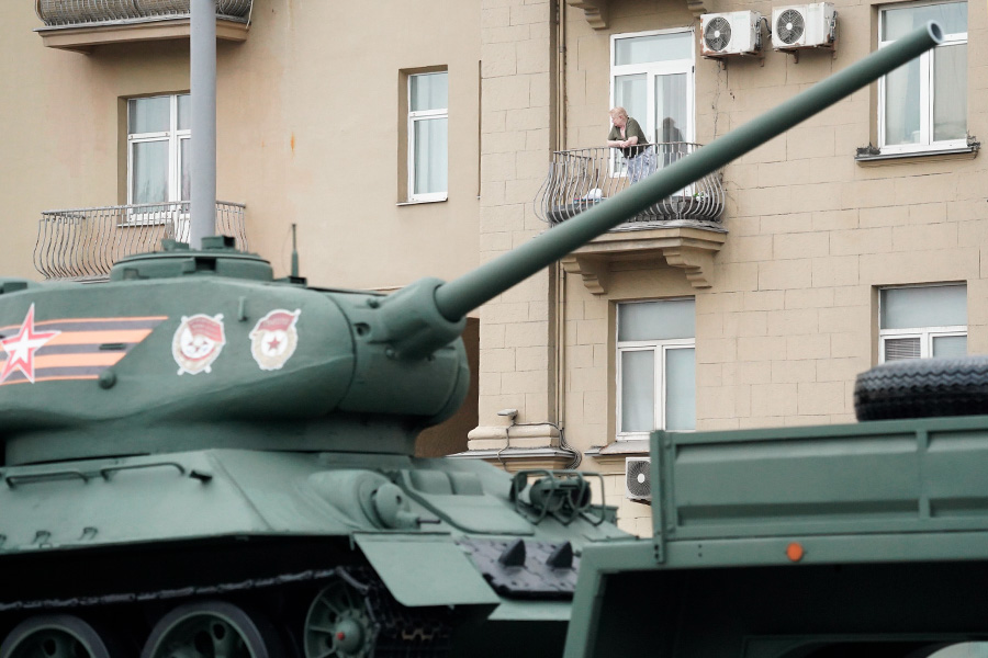 Женщина наблюдает за проездом военной техники с балкона своего дома