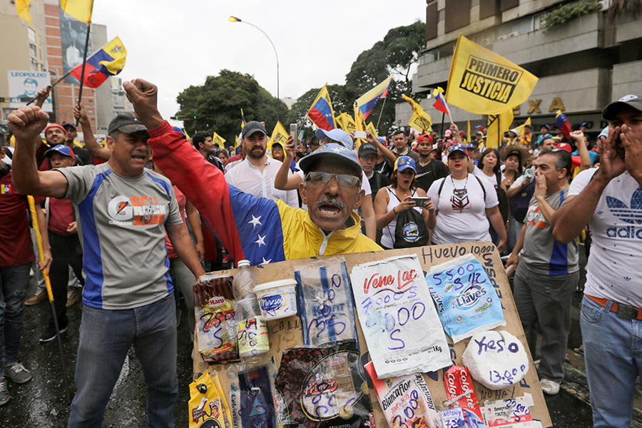 Участник оппозиционнного митинга держит плакат с ценами на продукты. В Венесуэле дефицит продуктов питания и медикаментов. Минимальная зарплата в стране составляет $30 в месяц
