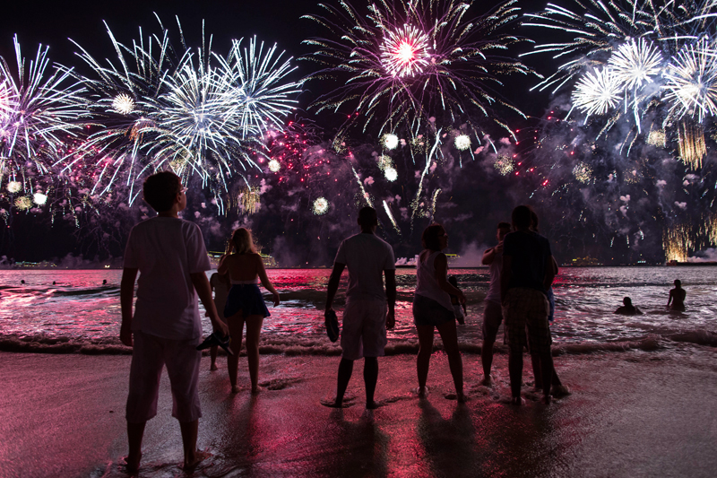 Люди смотрят на взрывы фейерверков во время празднования Нового года на пляже Копакабана в Рио-де-Жанейро.