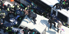 Полицейские пытаются задержать активиста, запрыгнувшего на крышу автобуса во время акции в поддержку экс-президента страны Пак Кын Хе
