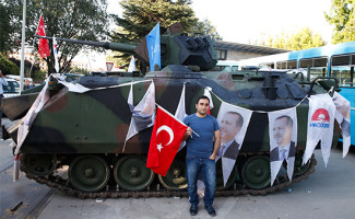 Сторонник действующего правительства позирует у захваченного танка мятежников возле парламента Турции в Анкаре
