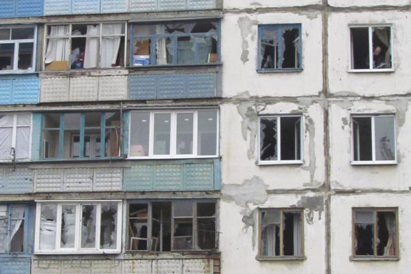 Люди выглядывают из окон жилого квартала в Мариуполе, подвергнувшегося артобстрелу