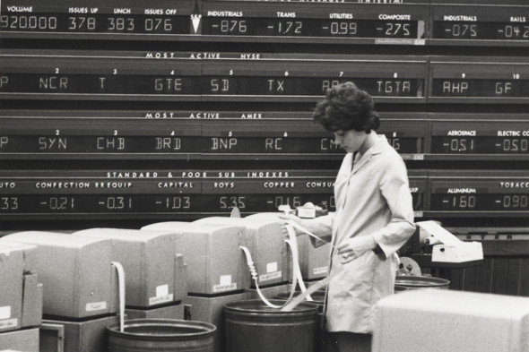 Stock Pricing, ca. 1960-1975
Photo of a woman looking at stock prices as they come out of the quotation machine. Wall of stock quotes behind woman.