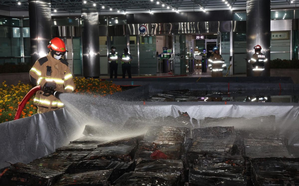 Пожарный обливает водой сгоревшие литий-ионные аккумуляторы после пожара в NIRS